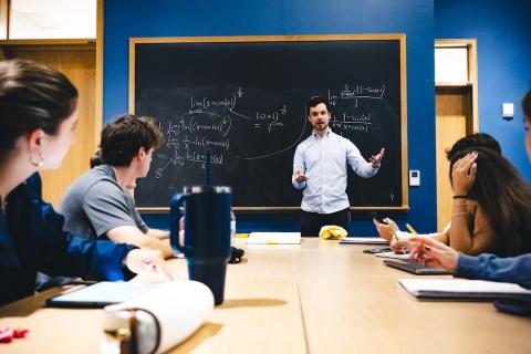 Isaac Reiter stands in front of a blackboard and tutors students.